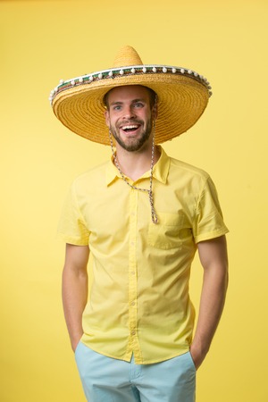 Man on smiling face posing in sombrero hat with hands in pockets, yellow background. Guy with bristle looks festive in sombrero. Fest and holiday concept. Man in festive mood going to celebrateの写真素材