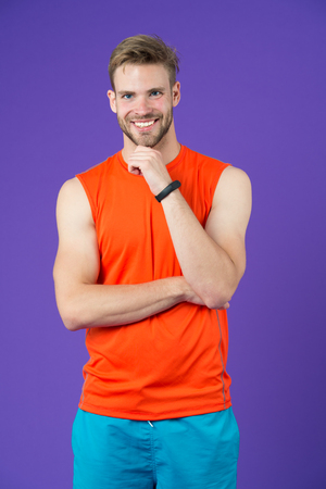 Happy man with sport smartwatch on violet background. Sportsman smile in orange vest and shorts. Fashion accessory for training. New technology for healthy lifestyle. Sport or fitness and wellnessの写真素材