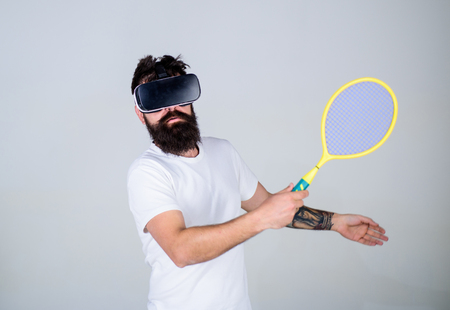 Guy with VR glasses play tennis with racket and ball. Man with beard in VR glasses beating pitch,...