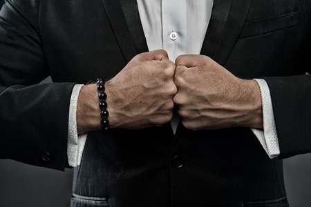 Male fists with swollen veins and bracelet on formal suit background. Confrontation concept. Hand of business person confronts against each other. Symbol of strength of willの写真素材