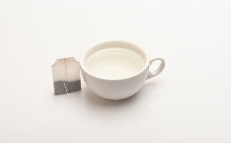 Mug filled with boiling water and teabag on white background. Process of tea brewing in ceramic mug. Tea time concept. Cup or white porcelain mug with transparent hot water and dry bag of tea nearの写真素材