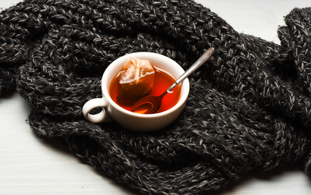 Mug filled with boiling water, teabag and spoon on knitted scarf background. Tea cup and dipped bag of tea wrapped with knitted scarf. Autumn drink concept. Process of tea brewing in mugの写真素材