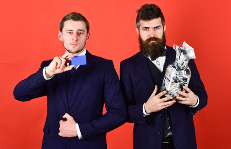 Men in suit, businessmen with jar full of cash and credit card, red background. Mature man and modern guy prefers different ways of saving, electronic money and cash. Safety savings conceptの写真素材