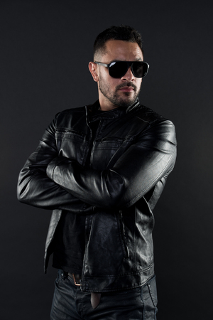 Confident man stand with arms folded. Bearded man in trendy sunglasses. Fashion model in leather jacket and jeans. Fashion and style. Confidence with sexuality and charismaの写真素材