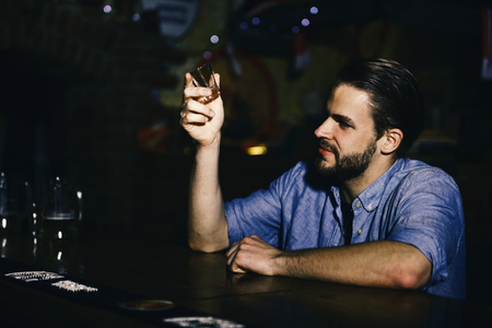 Alcohol addiction, loneliness. man sits in bar with empty shot glass in hand.の写真素材