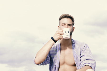 Sexy serious young macho holding cup of tea.