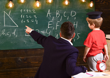 Young male teacher guides his child student to learning while pointing and looking at chalkboard...