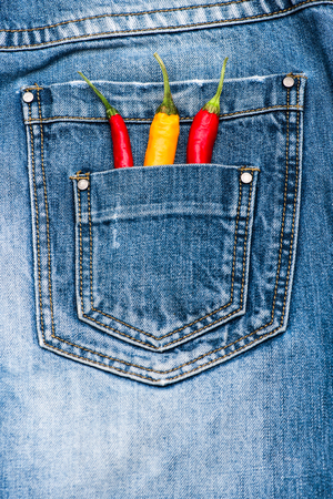 Pocket of jeans staffed with red and yellow chilly peppers, denim background. Peppers in back pocket of blue jeans. Piquant secret in pocket of pants, top view. Hot sensations conceptの写真素材