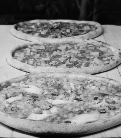 Pizza circles with meat, tomatoes and cheese on yellow wood background. Italian pizza and pizzeria concept. Take away food with various ingredients and crunchy edgesの写真素材