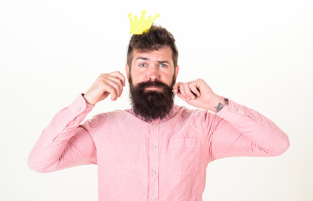 Mature bearded man with silly look playing king at birthday celebration, fun concept. Hipster in pink shirt with paper crown twirling mustache. Man with trendy beard posing with party accesssoriesの写真素材
