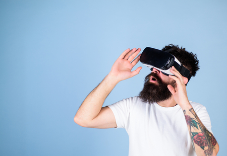 Man with long beard in VR goggles amused with new multidimensional experience. Hipster with trendy beard testing virtual reality headset isolated on blue background. Bearded man checking new gadgetの写真素材