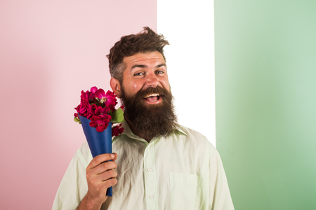 Flowers delivery concept. Man with beard cheerful face holds bouquet fresh flowers. Hipster with beard ready holiday congratulate. Guy holds bouquet confident about date. Delivery man with flowersの写真素材