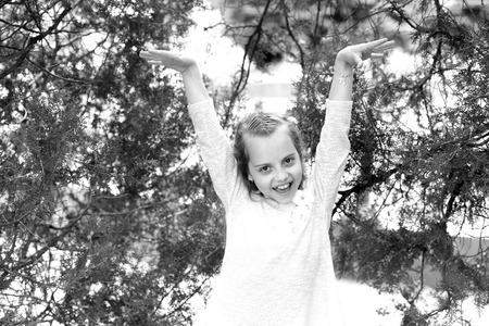 Happy girl in fashion dress pose at green tree. Little child smile with long blond hair outdoor. Kid model with fresh face skin in summer nature. Fashion beauty and hairstyle. Skincare and freshnessの写真素材