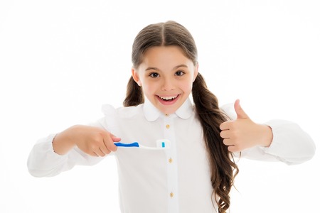 Girl cute long curly hair holds toothbrush white background. Child girl holds toothbrush with paste and shows thumbs up. Child school girl smart kid happy face cares hygiene. Brush teeth conceptの写真素材
