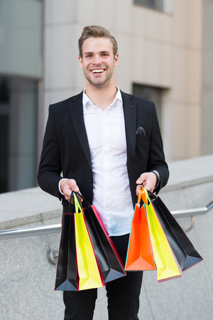 Man stylist professional shopper. Clothes courier. Stylist buy fashionable clothes client. Shopping service concept. Man formal suit shopping mall. Shop assistant helps carries bunch shopping bagsの写真素材