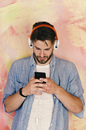 Cheerful teenage boy listening songs via earphones. European guy have fun time. Musical lifestyle. American handsome bearded man with headphones. Blue eyed stylish hipster with smartphone.の写真素材