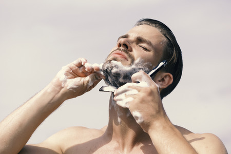 Man with bristle on clear sky background. Macho shaving chin with razor on clear sky backgroundの写真素材