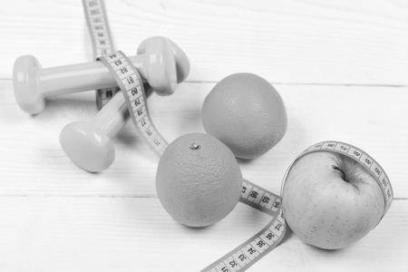sport and health concept, dumbbells weight with measuring tape, orange and apple fruit on white vintage wooden backgroundの写真素材