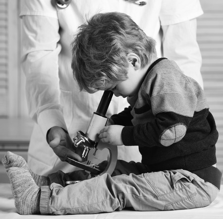 Boy does experiments on wooden background. Man and kid with busy face playing doctor or scientist.の写真素材