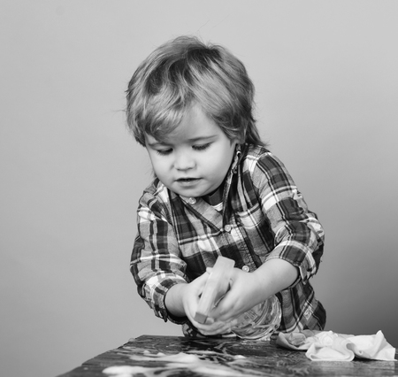 Kid near wooden table with rag and foam on.の写真素材