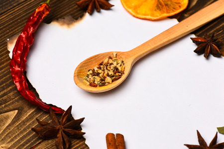 Piece of paper on wooden background. Spices, kitchen herbs lay around white paper. Cinnamon, dried...