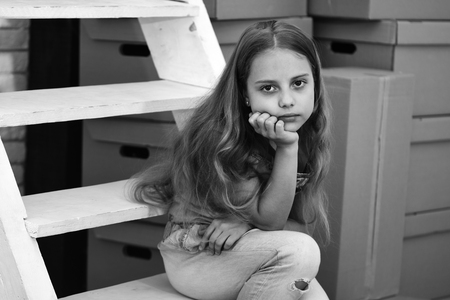 Kid sits on white ladder by pile of cardboard boxesの写真素材