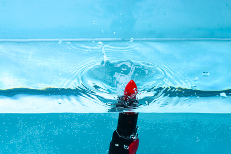 Water resistance cosmetic concept. Lipstick under water with transparent bubbles and splashes of liquid. Water resistant red lipstick fall into pur, transparent water, blue backgroundの写真素材