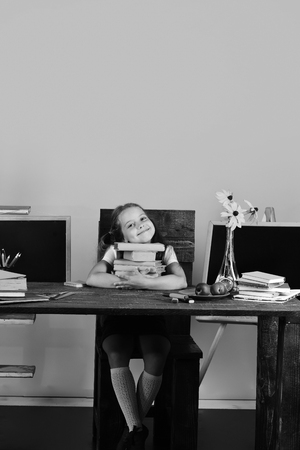 Childhood and back to school concept. Girl sits at desk with colorful stationery, flowers and fruitの写真素材