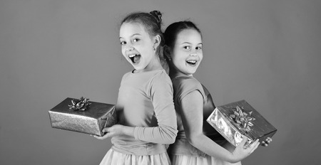 Girls with excited faces pose back to back with presents on green background. Children open gifts for Christmas. New Year presents concept.の写真素材