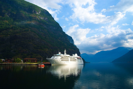 Cruise ship in sea port on mountain landscape in Flam, Norway. Ocean liner in sea harbor with green mountains. Cruise destination and travel. Summer vacation and holiday. Wanderlust and discoveryの写真素材