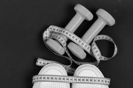 Fitness equipment. Pink dumbbells, measuring tape and sneakers on black background. Concept for healthy lifestyle, sport or fitness. Jogging and sportswearの写真素材