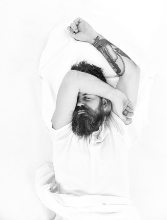 Morning and wake up concept. Man with sleepy face lies on pillow, white sheets.の写真素材