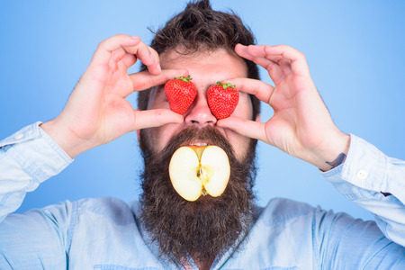 Fruit filling. Hipster surprised enjoy fruit filling. Man stuffed apple. Man handsome hipster long beard eat apple hold strawberry. Apple mouth bearded hipster holds strawberries in both handsの写真素材