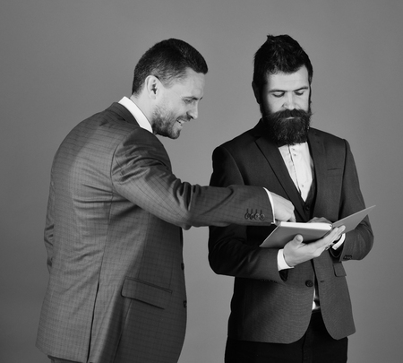 Businessmen with beards discuss business looking into notes. Machos in classic suits talk about schedule. Men with smiling faces read blue book.の写真素材
