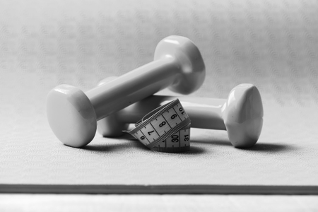 Shaping and fitness equipment. Dumbbells and measure tape in cyan blue color on purple background, close up. Sports and healthy lifestyle concept. Barbells next to roll of tape measure.の写真素材