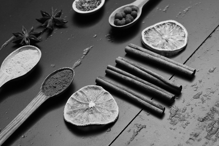 Wooden spoons with paprika, turmeric, herbs and pepper by cinnamon, anise, dry orange slice and chili. Composition of condiment, close up. Set of spices on dark grey wood background. Food art concept.の写真素材