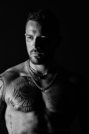 Sportsman or athlete with stylish beard and hair. Man with sexy muscular torso. Bearded man with tattooed chest. Fit model with tattoo design on skin. Bodycare or wellness and sport, black and whiteの写真素材