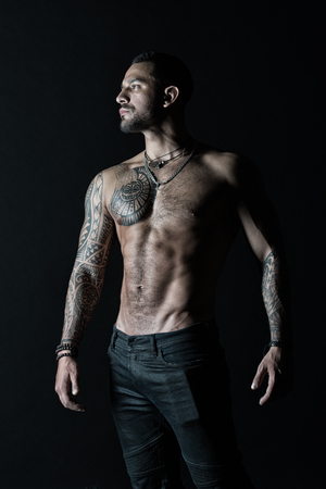 Tattooed man show sexy muscular torso. Sportsman with six pack and ab. Bodybuilder with biceps and triceps. Fashion model with tattoo in jeans. Bodycare with fitness and sport in vintage filterの写真素材