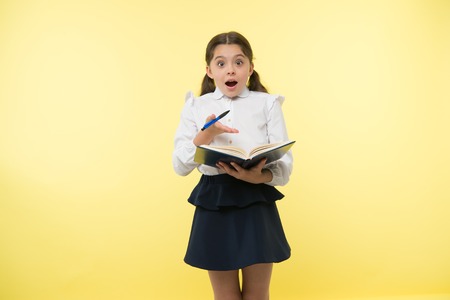Little child with surprised look. Schoolgirl with long hair hold book with pen. Fashion genius. Back...