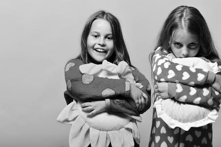Friends in pink pajamas isolated on pink background. Girls with loose hair hug their pillows. Childhood and friendship concept. Kids with smiling and grumpy faces hold green and yellow sun pillows.の写真素材