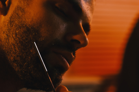 Man with bristle and dreamy face on defocused background. Macho shaving chin with razor. Sexuality and healthcare concept. Guy in bathroom with romantic light.の写真素材