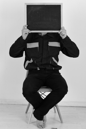 Mechanic or repairer holds blackboard with copy space. Service and construction presentation concept. Plumber in special costume. Man with beard holds empty chalkboard on white background.の写真素材