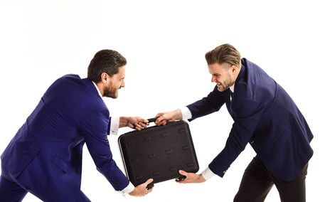 Businessmen or men in classic suits pulling from each other black briefcase. Partners with aggressive faces hold case on white background. Business conflict concept. Business rivalry between managers.の写真素材