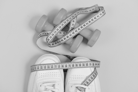 Sport shoes and equipment for healthy shape. Fitness and sportswear concept. Sneakers with measuring tape on yellow background. Centimeter in cyan blue color on trainers and pink dumbbells, top view.の写真素材