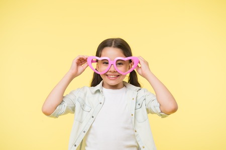 Happy child wear heart shaped glasses on yellow background. Little girl smile in fashion accessory. Summer fashion look. Funky style beauty. Young and confident. Valentines day. I love youの写真素材