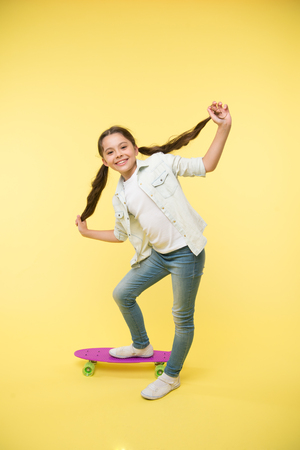 happy girl hipster show long brunette hair on penny board on yellow background. Little child smile with new hairstyle. Proud of her healthy hair. Beauty on skateboard. Beauty salon. Style and energyの写真素材