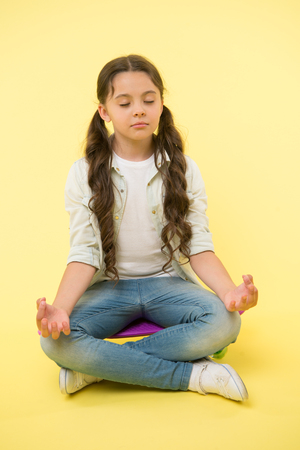 Little girl meditate sitting on penny board on yellow background. Time for yoga. Hipster child activity. Concentration and meditation. Staying calm. Skating is her life.Relaxation exerciseの写真素材