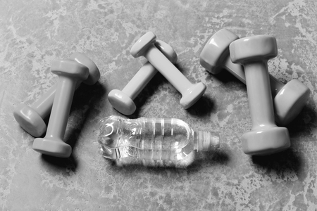 Shaping and fitness. Workout and sport concept. Dumbbells made of pink, green and cyan plastic on grey texture background. Barbells of different colors and water bottle placed in pattern, top view.の写真素材