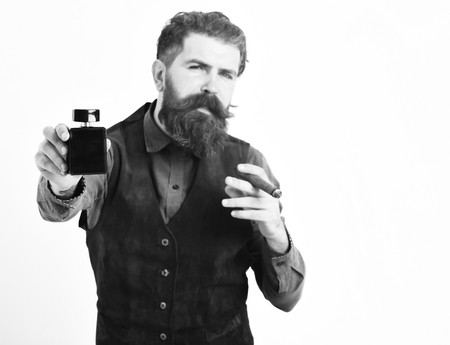 bearded man, long beard, brutal caucasian hipster with moustache smoking cigar with serious face and holding perfume isolated on white backgroundの写真素材