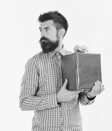 Surprise and holiday gift concept. Man with beard and curious face looks aside isolated on white background. Macho with wrapped blue gift and white bow. Guy in plaid shirt holds present box.の写真素材